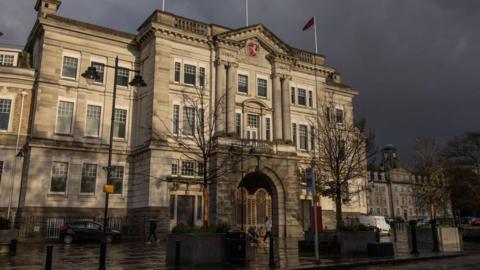County Hall in Maidstone, which is a large and grand stone building. Dark clouds are gathering in the sky above the building.