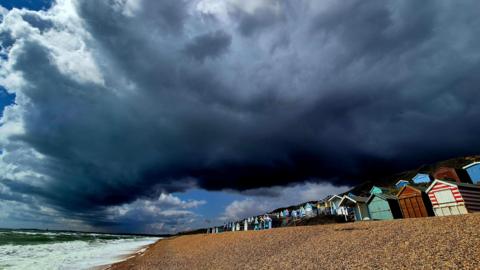 Milford on Sea, Hampshire - beach with huts in a row and low dark clouds rolling in.