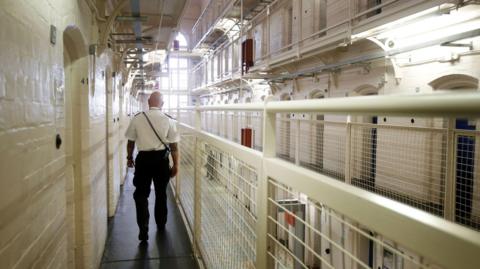 A prison guard walking in a prison surrounded by white railings.