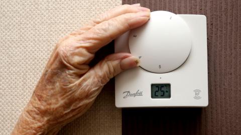 The hand of an elderly woman turning the dial of a white thermostat.