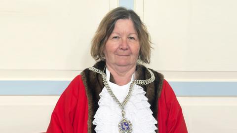 A woman with shoulder-length brown hair. She is dressed in mayoral robes and a chain of office.