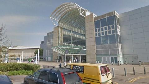 An image of the outside of a shopping centre in Bristol, captured via Google Maps. There are two cars parked outside including a yellow van.