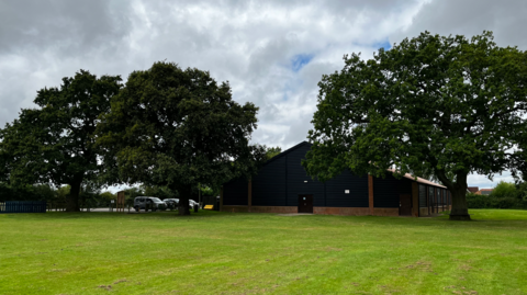 Three oak trees stand in a field next to a village hall