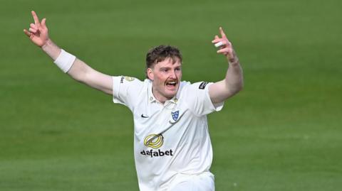 Sussex bowler Sean Hunt celebrates with hands aloft after taking a wicket