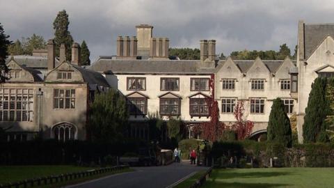 A front-on view of Coombe Abbey, a four-star hotel. The photo is taken from the other end of the hotel's drive, showing grass and trees leading up to the hotel.