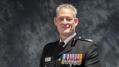 A head and shoulders picture of Mark Matthews, who is wearing an officer's uniform with medals. The background is a photography studio.