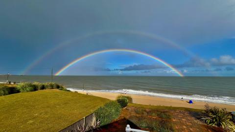 looking out across out over a beach to sea with some sunny spells with a full double rainbow