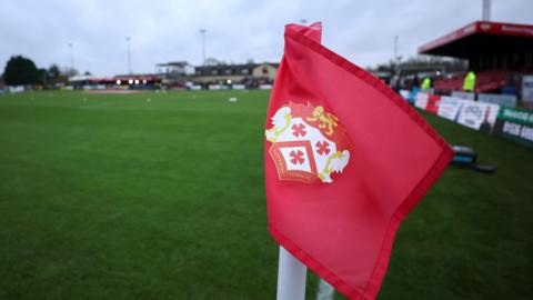 Kettering Town logo on a red corner flag at a gloomy Latimer Park stadium.
