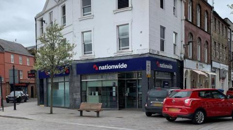 A Nationwide branch with cars parked around it and a bench in front