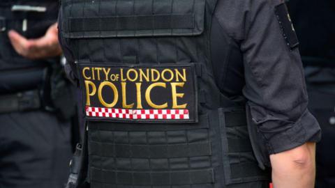A City of London Police officer uniform in gold writing with red and white checks