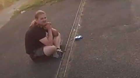 A man with hair in a pony tail sat cross-legged on the pavement.
