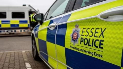 Essex Police car parked in a bay. There are the yellow and blue checks on the side of the car along with "Essex Police - protecting and serving Essex".