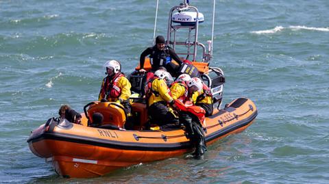 An orange RNLI lifeboat taking part in a mass rescue training exercise in Poole Bay. There are several lifeboat crew on board the RIB (rigid inflatable dinghy).