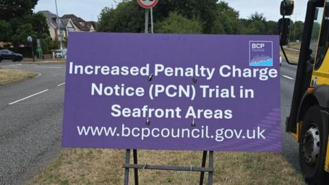 A purple sign saying Increased Penalty Charge Notice (PCN) Trial in Seafront Areas