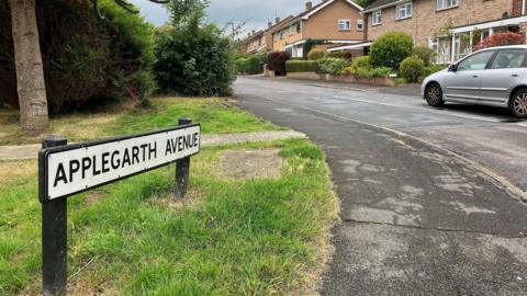 The entrance to Applegarth Avenue with the road sign and semi-detached houses in the background