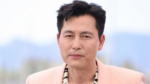 A photograph of Jung Woo-sung looking at the camera wearing a light pink blazer