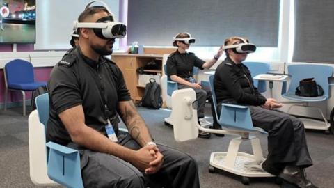 Three police officers sat in classroom chairs wearing virtual reality goggles