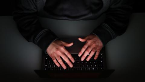 A man wearing black types on a black keyboard on a black table. You can only see his hands on the keyboard. 