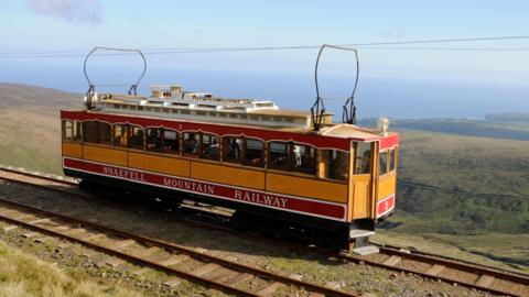 A snaefell mountain tram is high up on a hillside, in the distance you can see the sea.