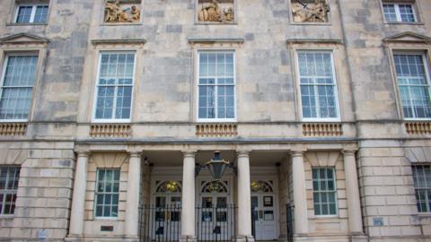 The exterior of Lewes Crown Court, a grey neo-Palladian building, made from Portland Stone, with columns in front of its main doors.