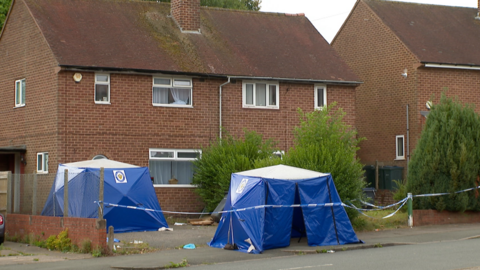 Two blue police tents, circles by police tape are placed on the driveway outside a red brick two storey semi-detached property