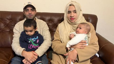 Nabeel Ahmed, sat on a sofa, with his wife and two children on a brown leather sofa. 