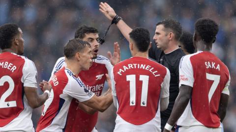 Leandro Trossard and Arsenal players surround referee Michael Oliver to protest about Trossard's red card.