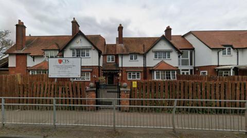 A Google Street imaghe of a two-storey white and red brick building with a wooden fence separating it from the path. There is a sign which says "CFS" on it.