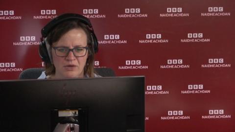 Shona NicEanraig ag aithris na naidheachdan