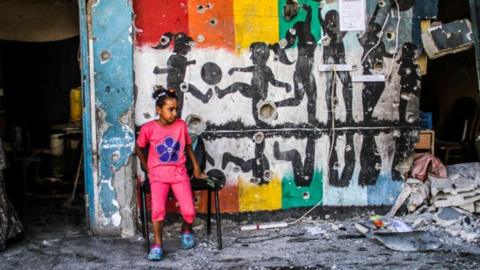 A girl dressed in pink sites outside the Al-Zeitoun C school after an Israeli air strike on 21 September