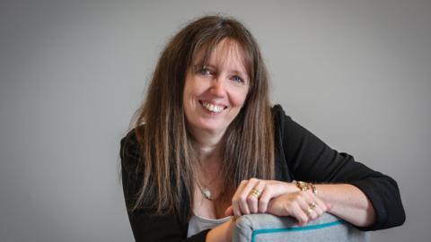 Samantha Everard sitting on a chair looking towards the camera with her arms folded.