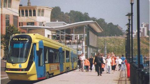 Artist impression of new tram system in Newcastle. The tram is yellow and people are walking next to it. It is pictured outside the Pitcher and Piano on Newcastle's Quayside.