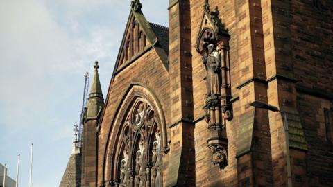 Dealbh de dh' Eaglais Chaluim Chille ann an Glaschu air là soilleir, le sgòthan gheal san adhar.