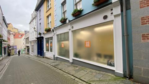 A grey street, with colourful buildings. 