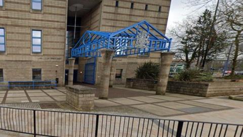 The front of Wolverhampton Combine Court, a light-coloured brick building with a large crest attached to a blue metal canopy which is supported by two brick columns.