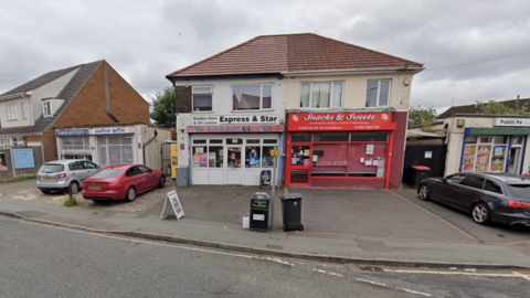 The store is pictured on the left with two cars parked nearby. It has a sign for the Express and Star newspaper above the shop and the frontage is white.
