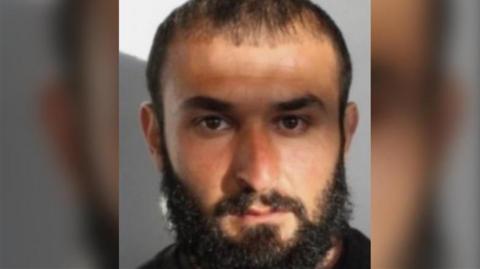 A custody image of a man with dark hair, a beard and a moustache.