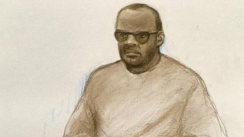 A court sketch of a man with glasses sitting down in the dock. He has receding short dark hair. 