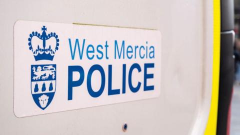 A sign on the side of a white vehicle door. The sign has blue writing that reads "west Mercia police" with a crown and a shield design 