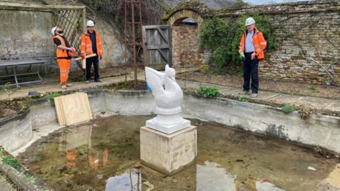 The stone swan sculpture positioned on top of a plinth with crane operators in the background 