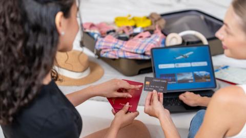 Two young women booking a flight online using credit card and passport - stock photo
