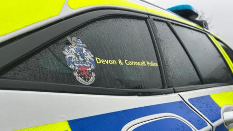Close up of a Devon and Cornwall Police vehicle. The police logo is on display on the window. Raindrops are running down the side of the car.