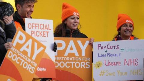 People holding signs reading "pay restoration for doctors"