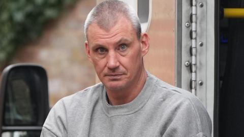 Donald Excell staring into the camera, he is in a grey prison issue jumper.