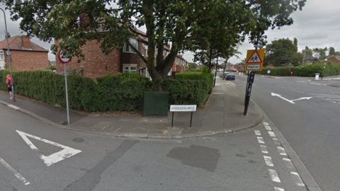 Endsleigh Drive in Middlesbrough. It is a residential road with lots of terraced houses lined in the street and several box hedges. There is a 20mph speed limit and a 'school patrol' road sign. 