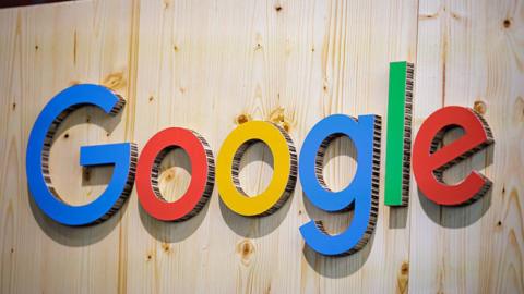 The Google logo (which is the word 'Google' with 'G' in blue, 'o' in red, 'o' in yellow, 'g' in blue, 'l' in green, and 'e' in red) on a wooden wall. The letters are made of cardboard.