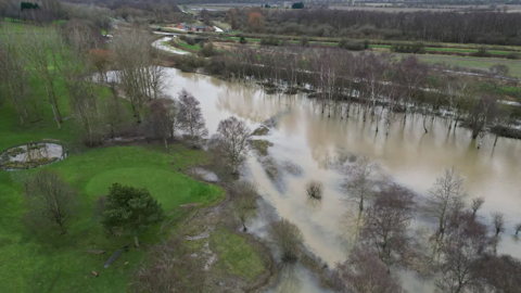 An aerial picture of part of Carholme Golf Course, with muddy water covering most of the scene. 
In the top right you can see the Foss Dyke Waterway. Its banks have broken.