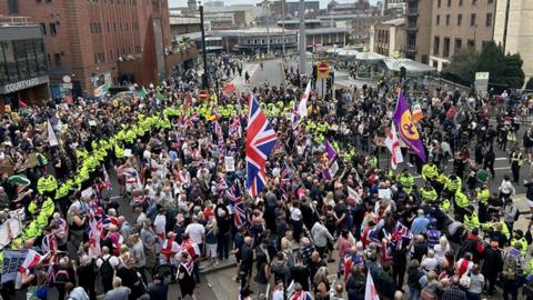 Crowds with flags attend the protest surrounded by police in high-vis jackets