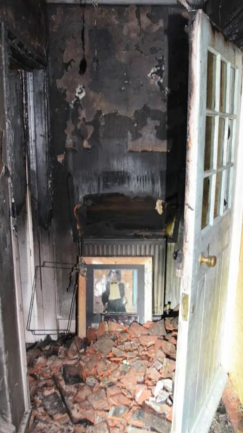 A burnt wall inside a house. There is rubble on the floor.