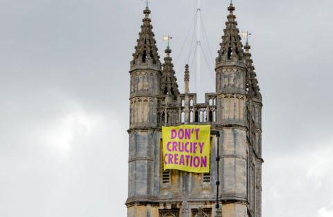The top of Bath Abbey's tower which has a large banner unfurled off it, saying "don't crucify creation"